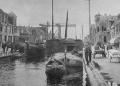 Een met turf geladen schip ligt in de sluis van Gorredijk om te worden geschut. Een langskomende bakker levert brood aan de schippersvrouw. (1931).