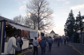 1983 Oktober, Najaarskermis Gorredijk in het jaar 1983 met deze keer vanaf de hoofdstraat (cafe/restaurant van der Zee) een inkijk in de Nieuwstraat daar waar veelal de eet/verkoop/behendigheid en altijd prijszaken een plaats vonden. Pal op de hoek (links op de foto) op over het algemeen de vaste plaats komen we een bekende kraam tegen namelijk de viskraam van de Gordykster Jelle van der Muur en zijn vrouw Minke. Het voelde als een reunie want de familie v...an der Muur had voor ze de vaste wal verlieten en verder gingen met de viskraam op kermissen en andere evenementen vele jaren een viswinkel in de Hoofdstraat van Gorredijk, om precies te zijn was hun winkel gevestigd op nummer 33. Naast de winkel werd er ook al gerezen met de kraam echter besloot van der Muur dat het na jaren lang de winkel gehad te hebben mooi was geweest. De winkel werd verkocht waarna de familie verhuisde naar Leeuwarden, ze zouden nog vele malen terugkeren naar Gorredijk, de plaats waar het allemaal begon en tenslotte hun roots lag. (Foto: Stichting Kermiscultuur)