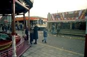 1983, Een inkijkje tussen de attracties door welke een standplaats hadden aan de Nieuwstraat tijdens de najaarskermis van Gorredijk in het jaar 1983. Met op foto links de bootjesmolen Speedway Carrousel van Nicholaas Rampen/van Nieff, erachter de Autoscooter van Cokkie Vermolen en op rechts de fotoschietsalon van Gosse Tilstra. (Foto: Stichting kermiscultuur)