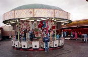 Een foto welke gemaakt is tijdens de Najaarskermis van Gorredijk in het jaar 1986 met afgebeeld één van de bekendste spelen van de kermis, namelijk de grijpkranen in dit geval de Holly Cranes van de bekende Nico & Angenes Sipkema & zonen Cornelis (Corry) & Hendrik (Henny). Nostalgie want hier begon het allemaal mee, veelal ronde tenten waar de nodige man uren in gingen zitten. De Holly Cranes van Sipkema had een diameter van 8 meter en bood plaats aan 20 speelkasten, de tent ...werd helemaal van de grond af opgebouwd en uitgepakt in zo'n 8 uren tijd. Grijpautomaten gaan binnen de familie Sipkema reeds generatie op generatie, Cornelis Sipkema senior liet de tent nieuw bouwen in het jaar 1966 en deed hem op zijn beurt in de loop der jaren over aan zoon Nico. Het was echter de tijd dat de inklapbare containers hun intrede namen op de kermis, ook binnen de familie Sipkema, welke veel minder arbeidsintensief waren wat betreft de opbouw en de afbouw. De tent werd in 1991/1992 doorverkocht aan de neef van Nico, Berend Sipkema welke er enkele jaren mee rees. In 1995 kocht de oudste zoon van Nico & Angenes, Corry Sipkema de tent terug en heeft er nog een melkbussenspel in geëxploiteerd. Op de foto runt de neef van Nico (Berend Sipkema) samen met de toen 16 jarige Henny Sipkema (Jongste zoon van Nico & Angenes) de zaak. Henny exploiteert hedendaags nog steeds grijpkranen op de kermis. De tent is na Corry verkocht aan Nicolaas Sipkema (zoon van Berend Sipkema) welke er een kikkerspel in exploiteert op kermissen in Duitsland. Naast de Holly Cranes is de bekende Autoscooter van de familie Sipkema te zien. (foto: SKC)